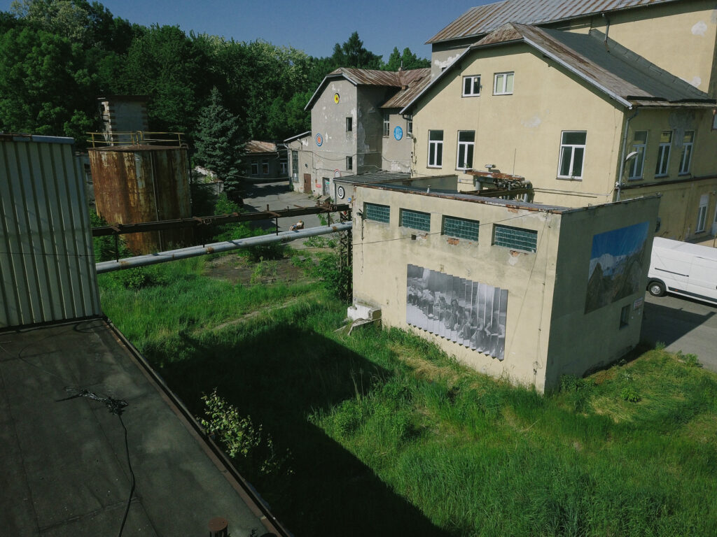 Widok na zabytkową Drożdżownię w Krakowie z kolażem archiwalnym umieszczonym na zewnętrznej ścianie budynku w przestrzeni postindustrialnej.