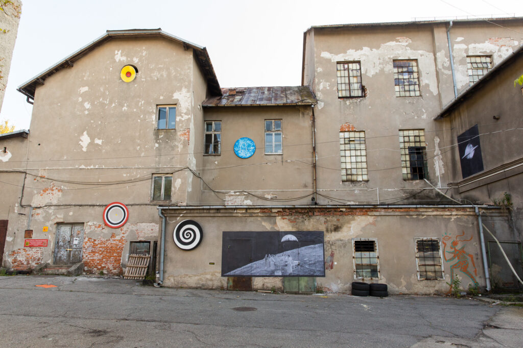 Elewacja zabytkowej Drożdżowni na Bieżanowie z instalacjami i archiwalnym kolażem na ścianie autorstwa Bartolomeo Koczenasz, Piotra Lutyńskiego i Adama Rzepeckiego