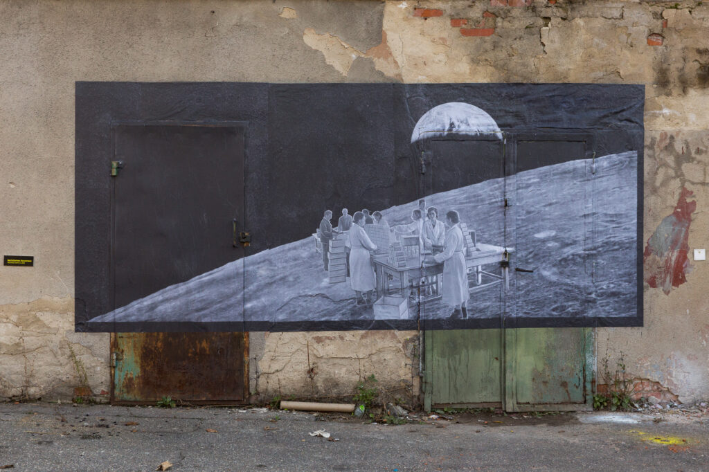 Kolaż na bazie archiwalnego zdjęcia z pracownikami fabryki zainstalowany na elewacji zabytkowej Drożdżowni w Krakowie.