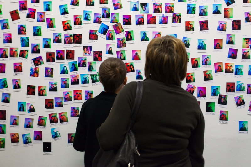 Visitor examining instant RGB self-portraits displayed on gallery wall, interactive installation view.