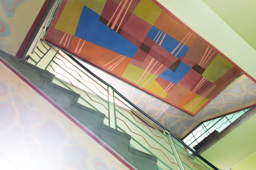 Organiczne linie i pastelowe formy malarskie na ścianie klatki schodowej.