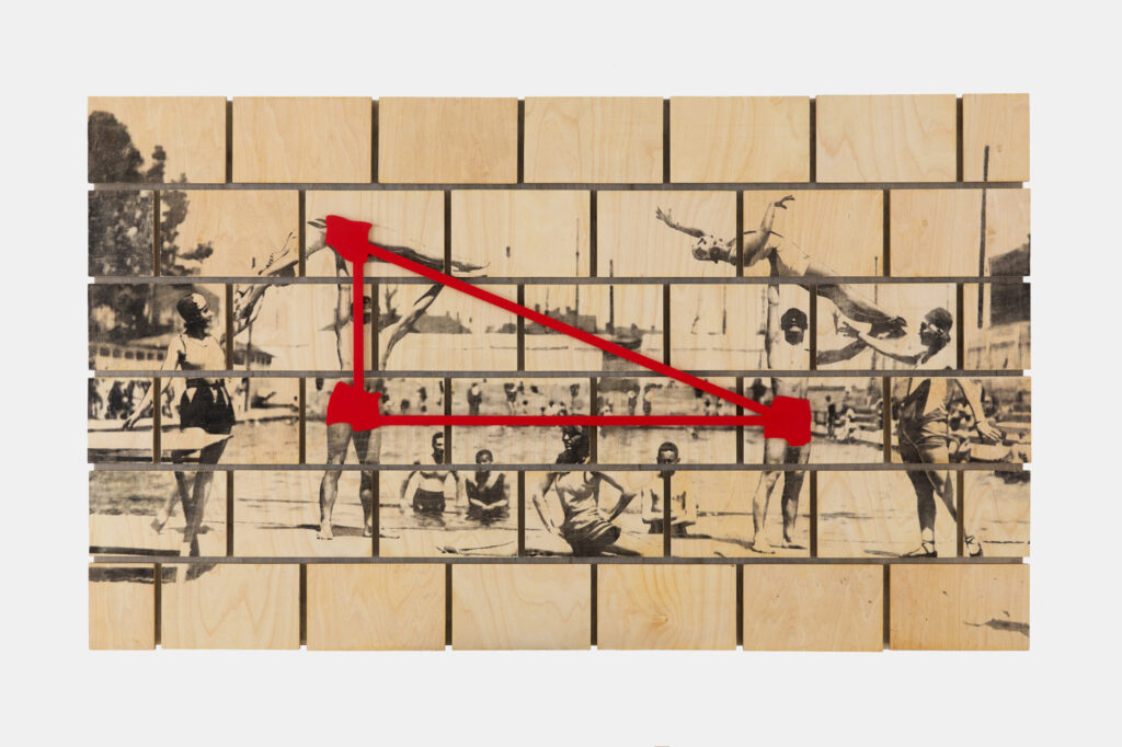 Asamblaż z drewnianych klocków z archiwalnym zdjęciem dawnego basenu w Parku Krakowskim w Krakowie oraz czerwonym geometrycznym znakiem na powierzchni pracy.