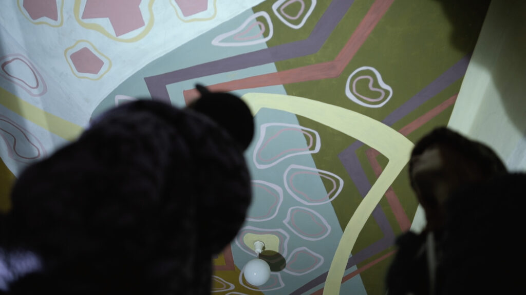 Odbiorcy oglądający sufitową realizację malarską w przestrzeni klatki schodowej.